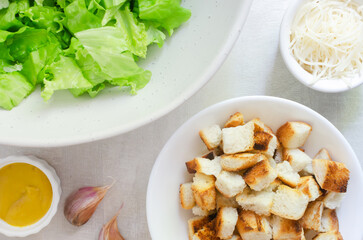 The process of cooking traditional Caesar salad with croutons and parmesan cheese on a gray table. The concept of traditional American cuisine. Horizontal orientation. Selective focus. Top view