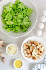 The process of cooking traditional Caesar salad with croutons and parmesan cheese on a gray table. The concept of traditional American cuisine. Horizontal orientation. Selective focus. Top view