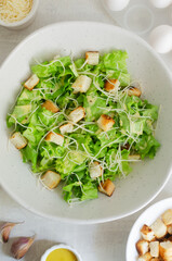 Traditional Caesar salad with croutons and parmesan cheese in a ceramic bowl with ingredients on a gray table. Traditional American cuisine concept. Vertical orientation. Selective focus. Top view.