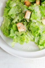 Traditional Caesar salad with croutons and parmesan cheese in a ceramic flat plate with ingredients on a gray table. Traditional American cuisine concept. Horizontal orientation. Selective focus. 