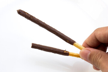 A hand holding chocolate stick biscuits on a white background.