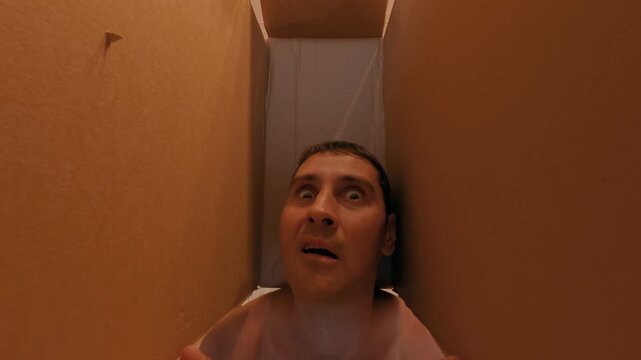 A man is threatened with a sharp knife, piercing the box containing his head. The guy is very scared seeing the big knife. A sense of danger.