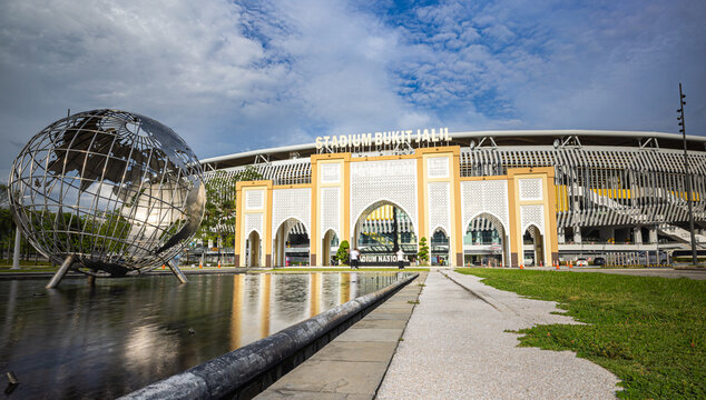 Kuala Lumpur, Malaysia &ndash; 16 September 2025: Bukit Jalil National Stadium facade with arched screens and a reflecting pool and steel globe sculpture under a bright sky. Low angle perspective