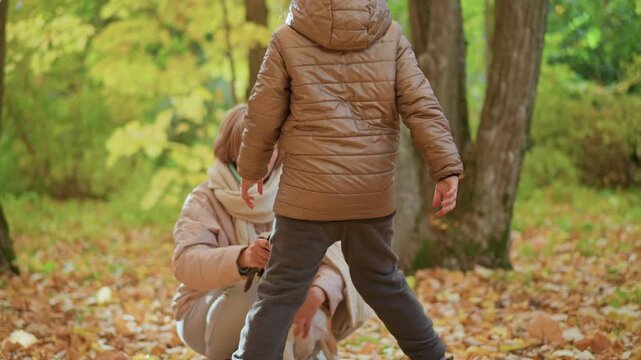 Little girl running through golden leaf carpet in autumn forest holding dog leash out to kneeling mother wearing coat and jeans, eager beagle sitting among trees in playful handover moment