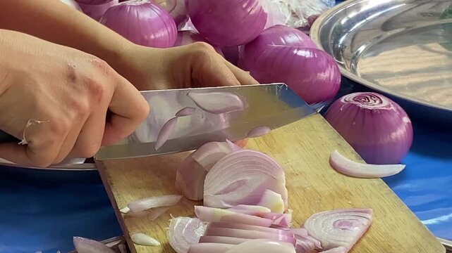 A woman hand uses a knife to cut an onion on a cutting board.