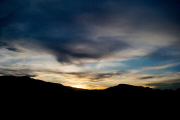 The last light of day casts a magnificent glow on the horizon, while the dark silhouettes of the mountains stand as stoic sentinels. 