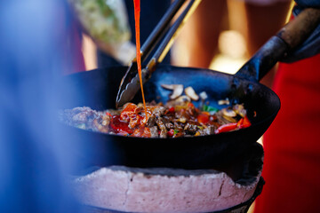 Close-up of colorful stir-fry cooking in outdoor skillet on brick stove