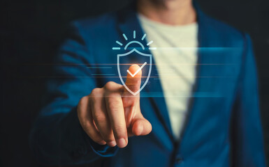 Businessman touching a virtual glowing shield icon with a checkmark and sunburst, symbolizing data security, protection, and verified digital wellness.