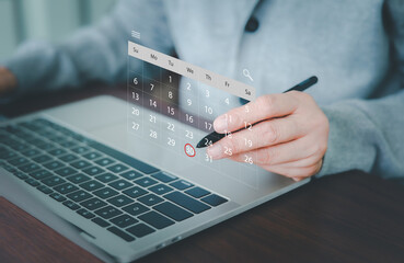A professional's hand is using a stylus, pointing to a virtual calendar projected over a laptop, with a specific date circled. Concept for efficient digital planning, time management, and deadlines.