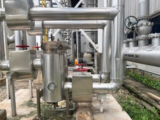 Complex industrial piping and valves at an outdoor processing plant. Stainless steel pipelines with...