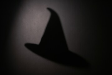 Fototapeta premium A shadow of a witch's hat cast on a dark background, evoking a mysterious and magical atmosphere.
