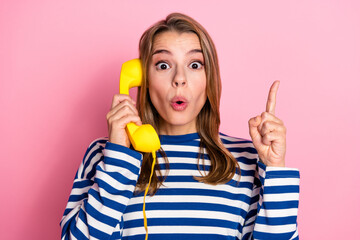 Surprised young woman talking on a retro phone, gesturing and expressing excitement against a trendy pink background
