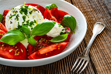 Caprese salad - tomatoes, fresh basil leaves and burrata cheese on wooden background	