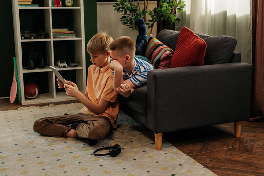 Two generation z boys using tablet and relaxing on sofa at home