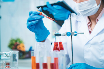 A gloved scientist carefully drips red solution into a flask, with red test tubes in the foreground, symbolizing precision, collaboration, and progress in modern medical dna blood research.