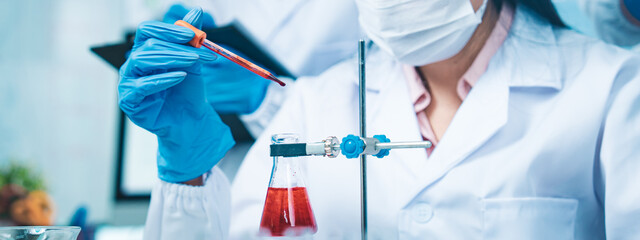 A gloved scientist carefully drips red solution into a flask, with red test tubes in the foreground, symbolizing precision, collaboration, and progress in modern medical dna blood research.