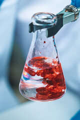 Close-up of a laboratory flask containing blood mixed in clear liquid, representing research, biotechnology, and medical analysis for discovering solutions to disease and healthcare challenges.