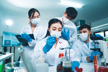A group of scientists collaborate in a laboratory, with a female researcher dropping blood sample...