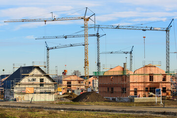 In einem Neubaugebiet stehen viele Baukräne vor Wohnhäuser im Rohbau, als Symbolbild für Wohnbau und Wohnungspolitik - digital bearbeitet