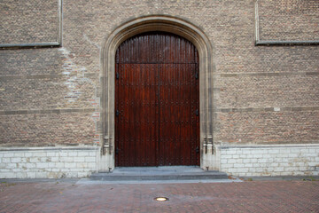 Large wooden door with intricate design stands prominently against a textured brick wall, showcasing architectural details and historical craftsmanship in a serene outdoor setting
