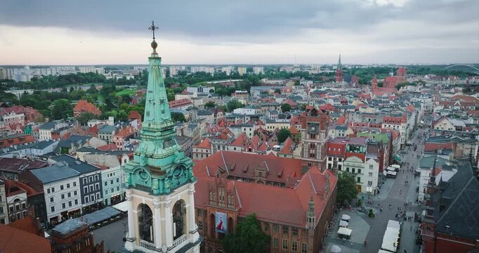A dynamic aerial shot flying in an arc around the Church of the Holy Spirit in Torun, Poland. The video captures the church tower in the foreground, with a panoramic view of the Old Town.