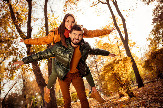 Happy couple enjoying a piggyback ride during a sunny autumn day with vibrant foliage and natural light in the park