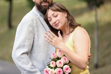 Making marriage proposal. Woman showing engagement ring and hugging her fiance outdoors