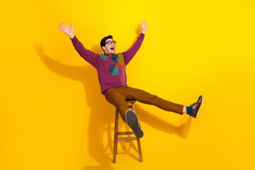 Obraz premium Young stylish man sitting playfully on a chair against a yellow background, expressing excitement