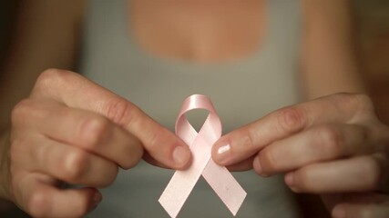 Close-up of female hand holding pink satin ribbon, symbolizing support for breast cancer awareness, medical care, and self-examination.