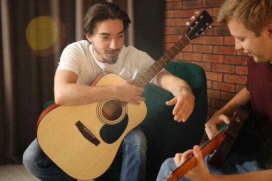 Tutor teaching man to play guitar indoors