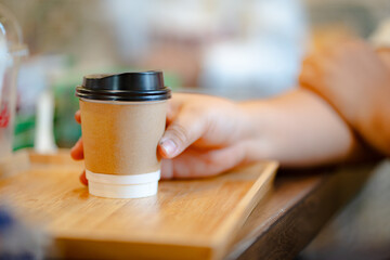 hand of woman holding a take-out hot coffee on wooden table