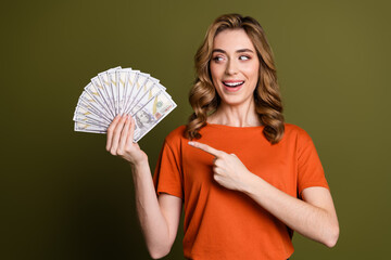 Smiling young woman holding fan of dollars, pointing towards wealth and financial success, promoting savings or rewards