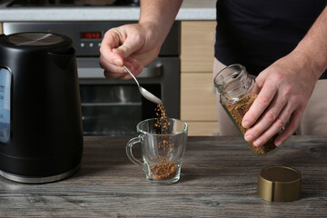 An adult man pours instant coffee into a glass cup and prepares a drink.