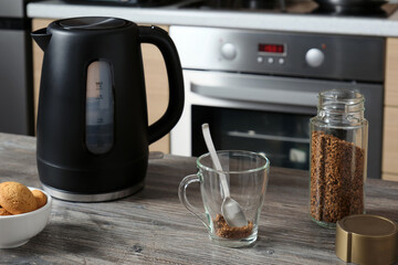 A glass cup, an electric kettle and a jar of instant coffee, cookies on the table.