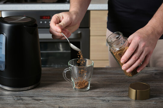 An adult man pours instant coffee into a glass cup and prepares a drink.