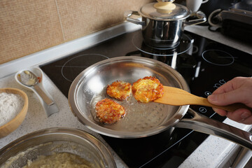 A man is frying potato pancakes in a steel pan against the background of home kitchen, cooking at home.