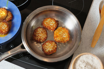 Top view potato pancakes are fried on top in a steel pan on an electric induction stove.