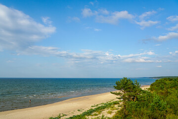 Scenic sandy Baltic sea beach with blue sea and cloudy sky, bordered by lush green coastal forest