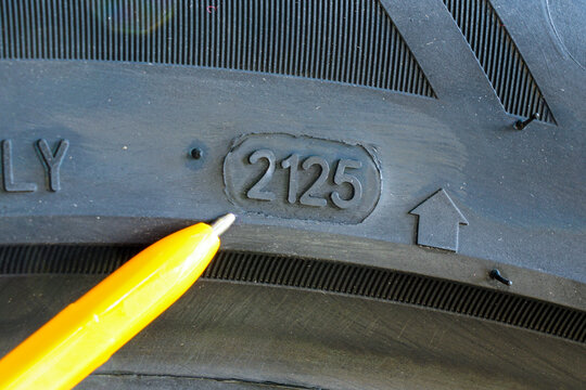 Close-up of tire sidewall showing DOT code 2125 production week and year marking with pen pointer