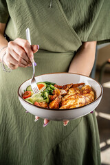 Woman holding a bowl with omelette, chicken, and salad.
