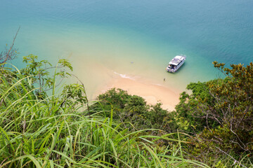 Defocused view through the grass to sandy beach and tourist motor boat on sea island. Background for travel on paradise nature