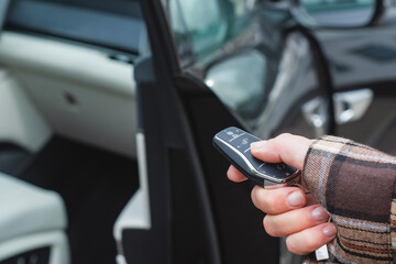 Obraz premium Close-up of a person holding a car key with a remote control in front of an open vehicle door. Concept automotive access, smart keys, car security and modern transportation.
