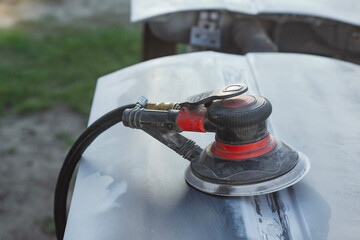 Close-up of an pneumatic orbital sander on a car body panel, used for sanding and surface preparation in automotive repair and restoration. Concept of car repair and auto bodywork.