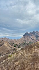 Experience the majesty of the vast rugged mountain landscape of Padar Island - Komodo National Park, showcasing rolling golden hills under dramatic cloudy skies.