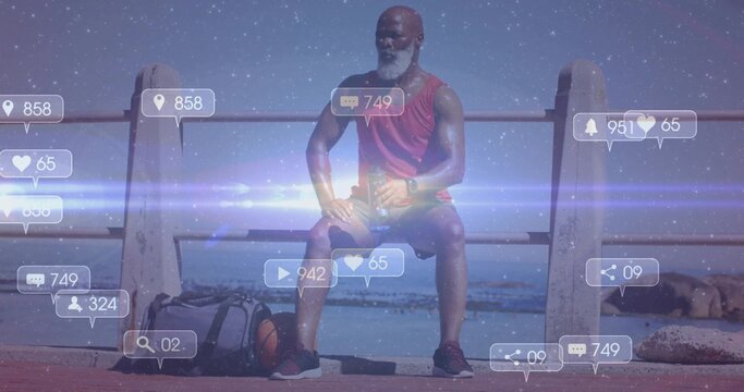 Sitting man wearing smartwatch on seaside promenade, with duffle bag, basketball, floating icons