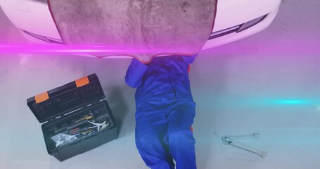 Repairing mechanic checking underside of white car on workshop floor, with toolbox and wrenches