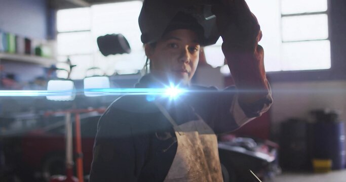 Lifting helmet visor female welder wearing heavy apron and gloves in garage, with welding arc flare