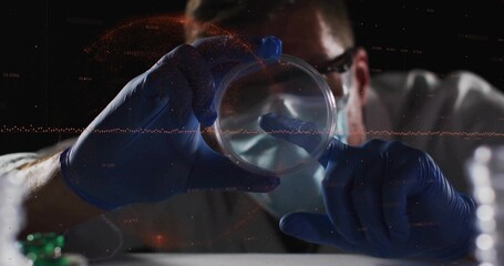 Examining scientist wearing lab coat mask glasses gloves holding petri dish at lab bench with vials