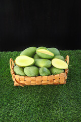 Fresh Green Mangoes in Wicker Basket on Grass with Cut Slices Showing Ivory Flesh