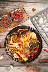 Spicy Fish Head Casserole with Red Chili Peppers and Fragrant Spices in Traditional Black Pot on Wooden Table